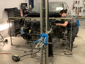 Maximum Collision employee in safety glasses working on damaged front end of a car